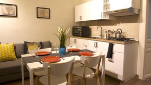 A modern kitchen with white cabinets, a black microwave, and a gas stove. There is a dining table with chairs and a potted plant.