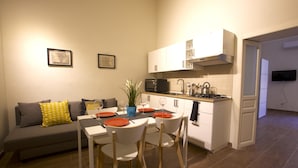 A modern kitchen with white cabinets, a microwave, and a gas stove. There is a dining table with chairs and a small potted plant.