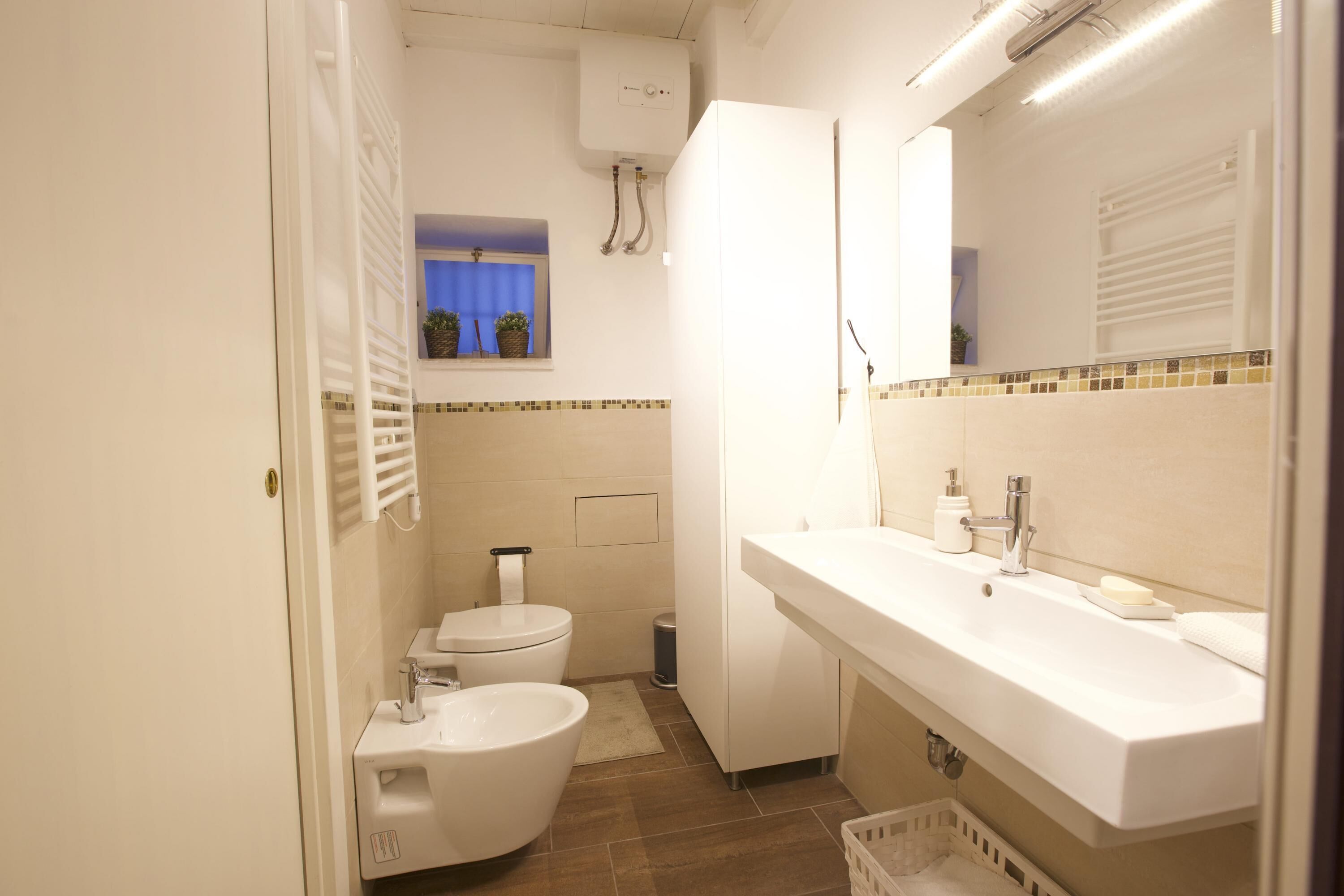A compact bathroom with a toilet, bidet, sink, and mirror.