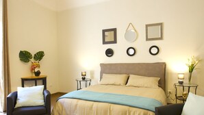A neatly arranged bedroom with a bed, two armchairs, a small table, and a bedside table with a lamp.