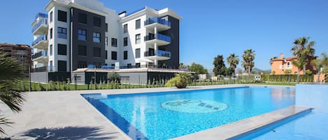 Un bâtiment moderne doté de balcons, d’une piscine et de palmiers.