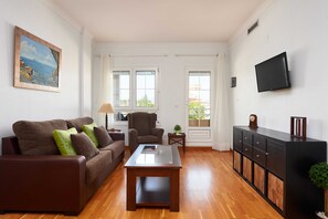 Een woonkamer met een bruine bank, een salontafel met glazen blad, een donkere houten kast en een flatscreen televisie die aan de muur is bevestigd.
