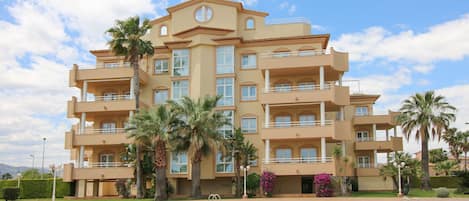 A multi-story hotel with a pool area, palm trees, and a clear sky.