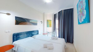 A hotel room with two beds, a small table, a chair, and artwork on the walls. - Fade by ON Travel (Oliva)