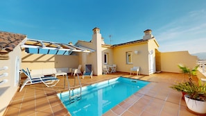 Ett poolområde på taket med en blå pool, vita solstolar och ett litet bord.