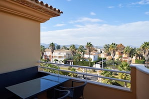 Un balcón con mesa y sillas, con vistas a una zona residencial con palmeras y casas.