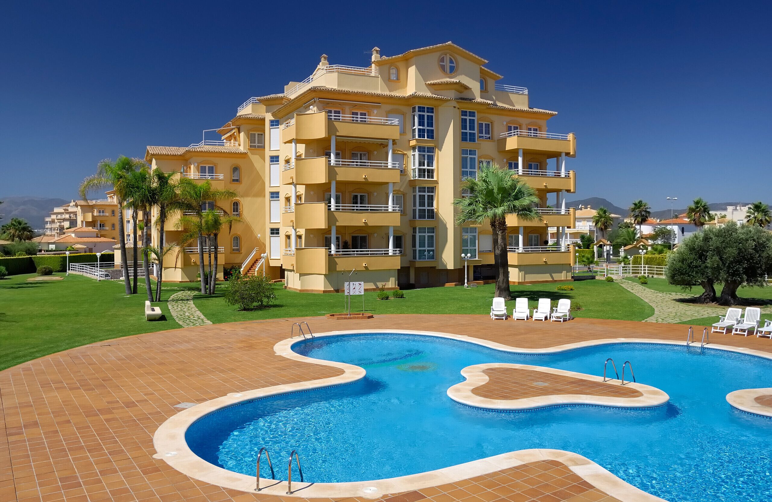 A hotel with a swimming pool, multiple balconies, and a well-maintained lawn.