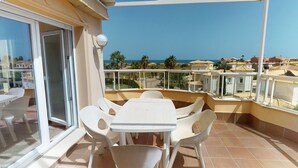 A balcony with a table and chairs, a glass door, and a view of the sea and neighboring buildings.