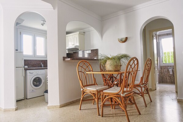A kitchen with a washing machine, a dining table with chairs, and a potted plant.