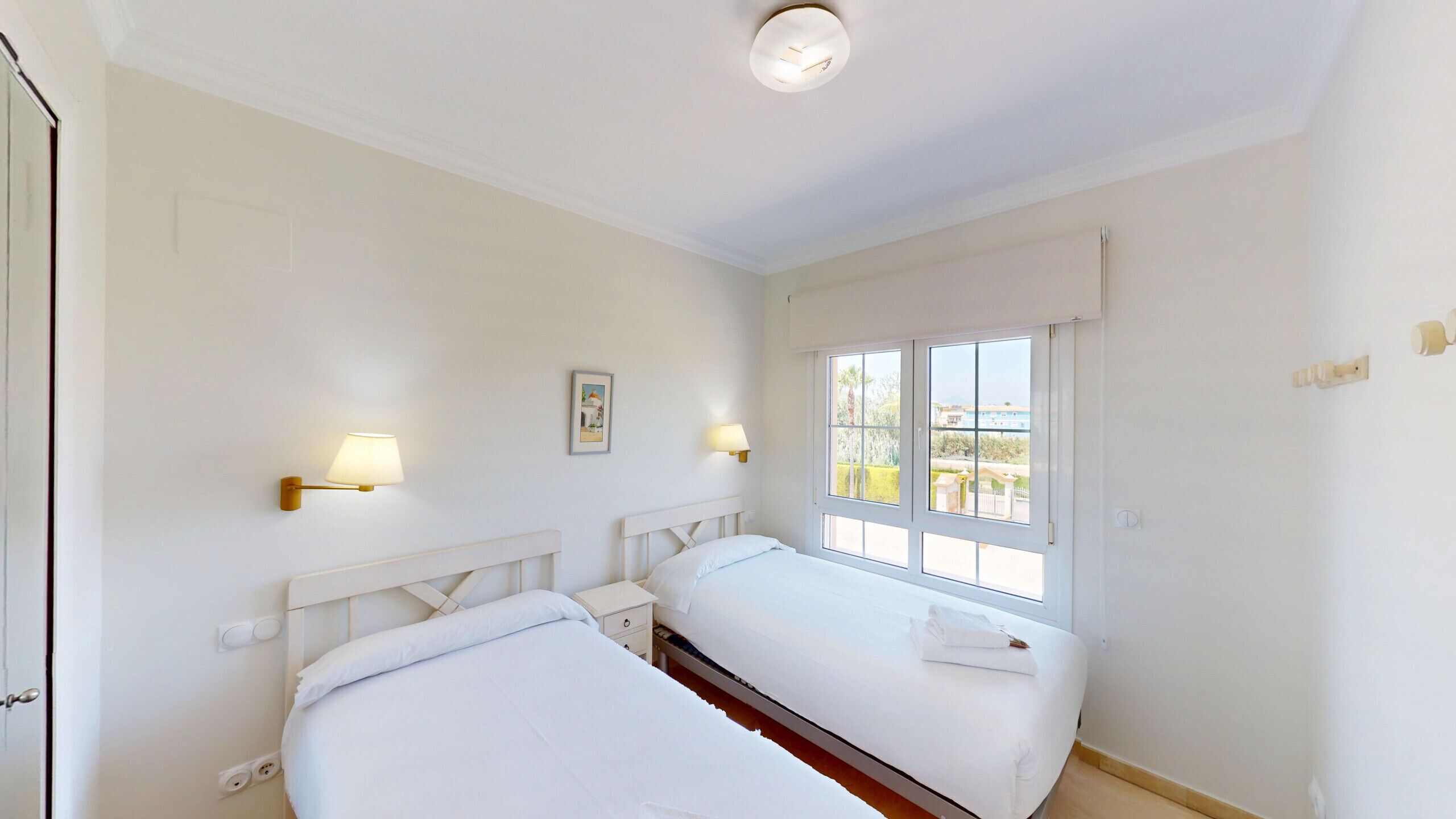 Une chambre avec deux lits, une fenêtre donnant sur un beau paysage et deux lampes fixées au mur.