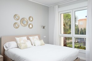 A bedroom with a large bed, a window with a view of greenery and buildings, and decorative wall mirrors.