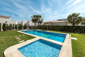A rectangular swimming pool with a tiled deck, surrounded by well-maintained grass and palm trees.