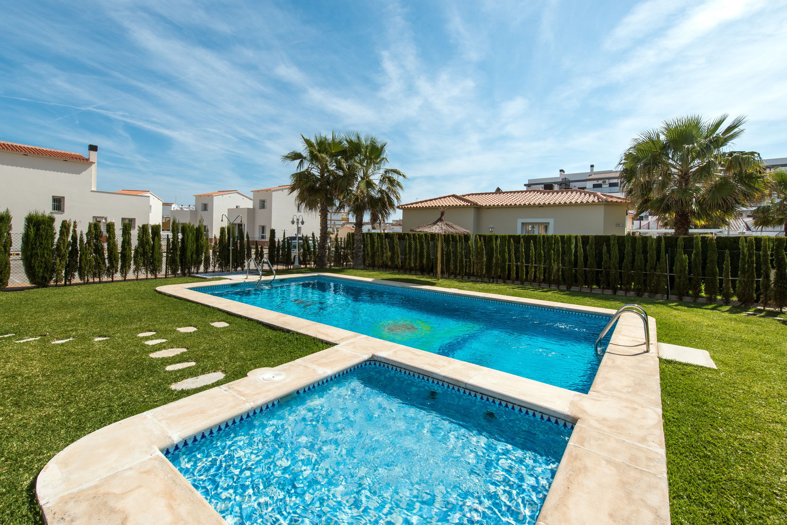 A rectangular swimming pool with a tiled deck, surrounded by a well-maintained lawn and a row of tall, narrow trees.