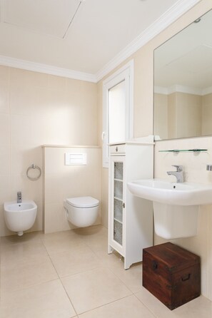 Une salle de bain comprenant des toilettes, un bidet, un lavabo et une petite commode en bois.