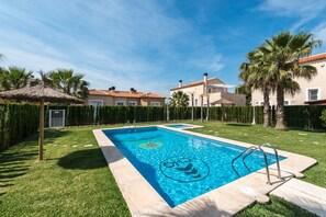 Une piscine à l’eau d’un bleu limpide, entourée de pelouse bien entretenue, de palmiers et d’une zone délimitée par une clôture.