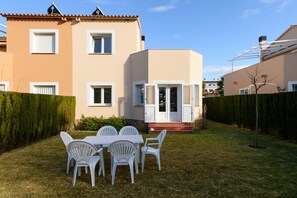 Un immeuble résidentiel doté d’un toit plat, d’une porte d’entrée et d’un petit jardin devant, avec une table et des chaises.