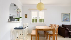 Uma área de refeições com mesa e cadeiras de madeira, um banco branco, uma planta em vaso e um quadro na parede.
