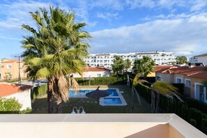 Un quartier résidentiel doté d’une piscine entourée de palmiers et, au fond, d’un ensemble d’immeubles.