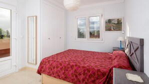 Quarto com cama, mesa de cabeceira, abajur, janela e porta.
