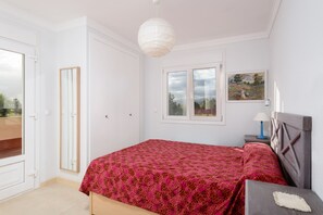 Une chambre à coucher avec un lit, une table de chevet, une lampe, une fenêtre et une porte.