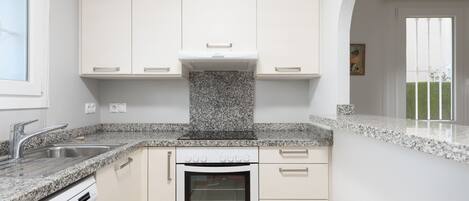 A modern kitchen with white cabinetry, granite countertops, a built-in oven, and a window with a view of a garden.