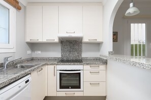 Una cocina moderna con muebles blancos, encimeras de granito, horno empotrado y ventana con vistas a un jardín.