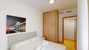 A hotel room with a bed, a wooden wardrobe, a door, and a wall-mounted picture of a bridge. - Lily by ON Travel (Oliva)