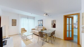 Un salon moderne comprenant un canapé, deux fauteuils, une table à manger en verre et un tableau représentant un paysage urbain.