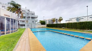 Une piscine rectangulaire dotée d’une terrasse en bois et d’un mur en verre sur l’un de ses côtés.