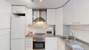 A modern kitchen with white cabinetry, a stainless steel range hood, a built-in oven, a microwave, a coffee maker, and a sink with a faucet.