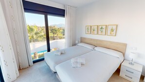 A hotel room with two beds, a large window with curtains, and a view of palm trees and mountains.