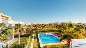 Una piscina rodeada de palmeras y un campo de golf, con edificios modernos al fondo.