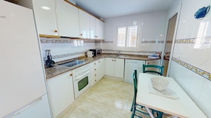 A kitchen with white cabinets, a granite countertop, a built-in oven, a sink, and a dining area with a table and chairs.