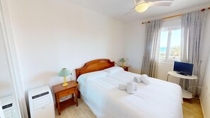 A hotel room with a bed, a TV on a small table, and a window with curtains.
