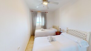 Ein Hotelzimmer mit zwei Betten, einem Deckenventilator und einem Fenster mit Vorhängen.