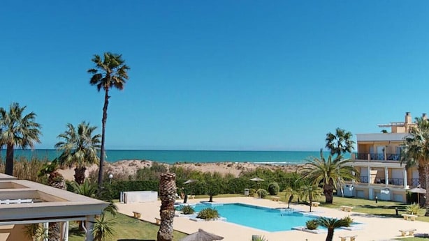 Una propiedad frente a la playa con piscina, palmeras y vista al océano.