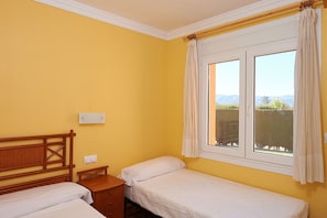 Una habitación con dos camas individuales, un cabecero de madera, una mesita de noche pequeña y una ventana con cortinas.