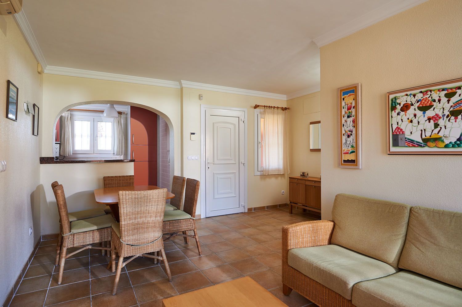 A dining area with wicker furniture, a sofa, and a painting on the wall.