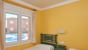 Una habitación con dos camas individuales, una ventana con cortinas, un cabecero de madera y una mesita de noche pequeña verde.