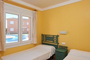 Ein Zimmer mit zwei Einzelbetten, einem Vorhangfenster, einem hölzernen Kopfteil und einem kleinen, grünen Nachttisch.