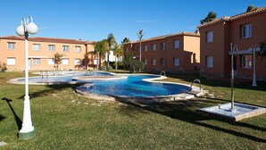 A pool area with a circular design, surrounded by well-maintained grass and palm trees. - Velvet by ON Travel (Oliva)
