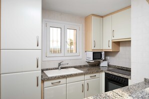 A kitchen with white cabinets, a granite countertop, a microwave, a sink, and a stove.