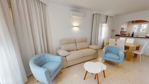 Un salon moderne comprenant un canapé, deux fauteuils, une petite table ronde et un coin repas avec une table et des chaises en bois.