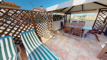 Une terrasse extérieure couverte, avec une table et des chaises, une clôture en bois et une vue sur les environs.