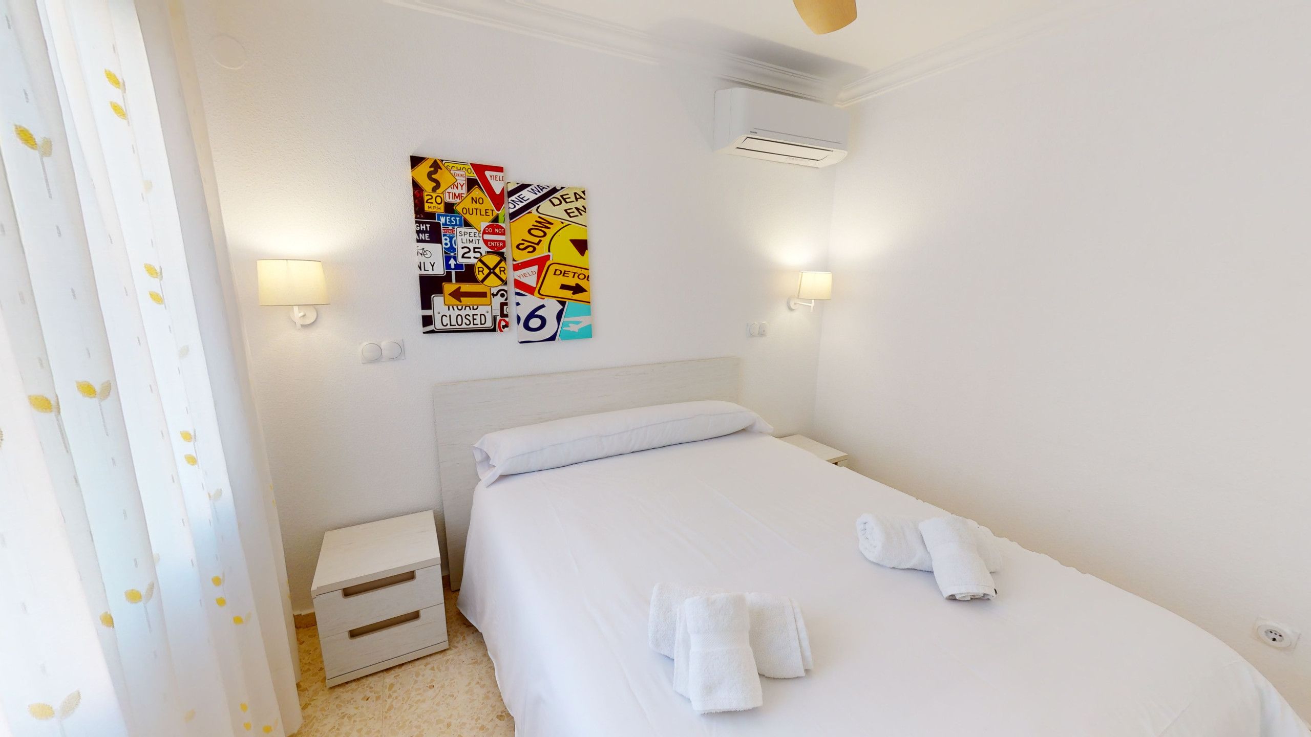 Habitación de hotel con cama, mesita de noche, aire acondicionado instalado en la pared y una pared con varios carteles.