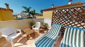 Une terrasse avec deux chaises longues à rayures, une petite table et deux chaises blanches.
