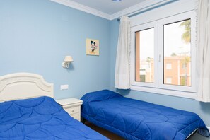 Ein Zimmer mit zwei Betten, einem Nachttisch, einer Lampe und einem Fenster mit Vorhängen.