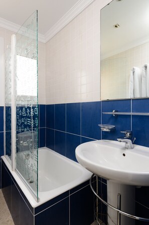 Un baño con cabina de ducha de vidrio, un lavabo blanco y paredes con azulejos azules.