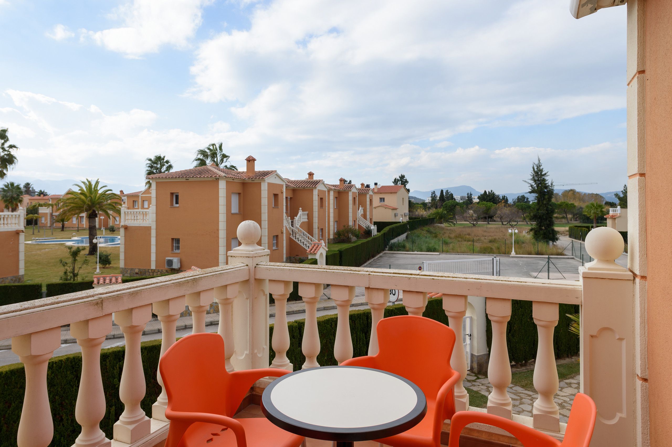 Ein Balkon mit orangefarbenen Stühlen und einem kleinen Tisch, mit Blick auf eine Wohngegend mit Häusern und einer Straße.