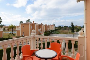 Un balcón con sillas anaranjadas y una mesa pequeña, con vista a una zona residencial con casas y una calle.